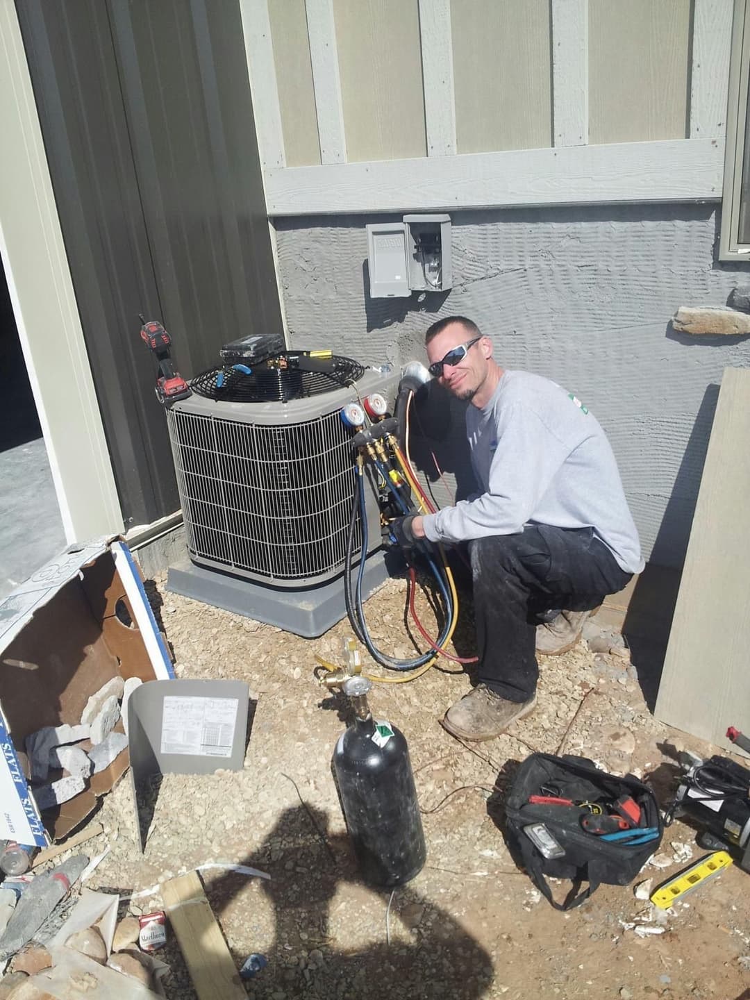 Technician repairing an air conditioning unit outdoors with tools and equipment nearby.