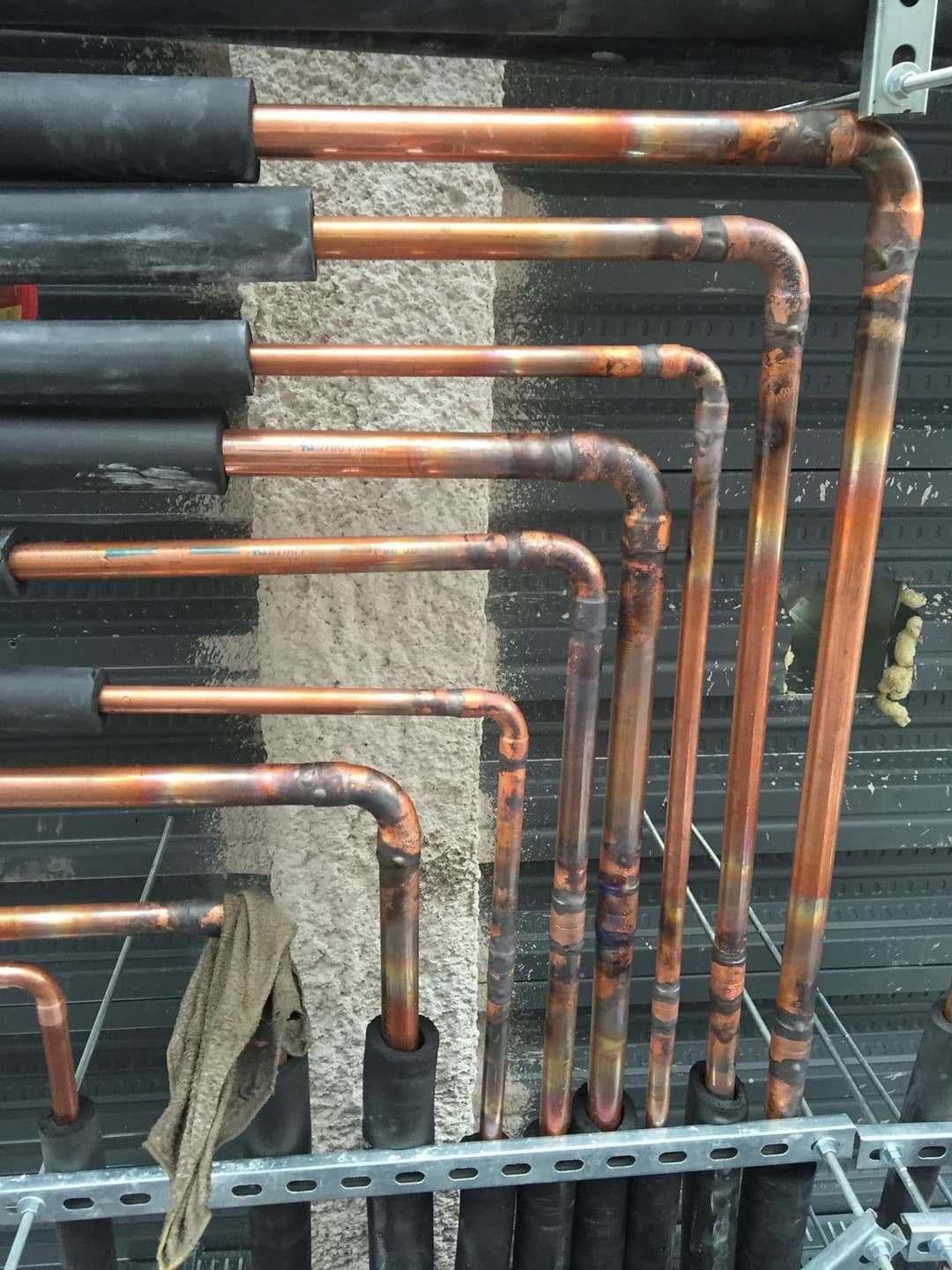 Copper pipes with joints and insulation installed on a wall, showcasing plumbing setup.