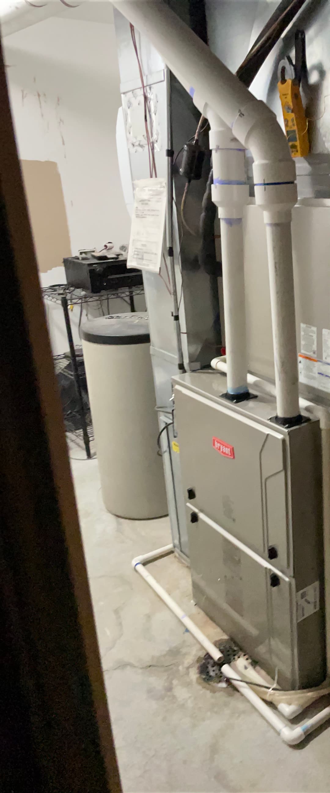 Furnace installed in a basement with white pipes and storage equipment nearby.