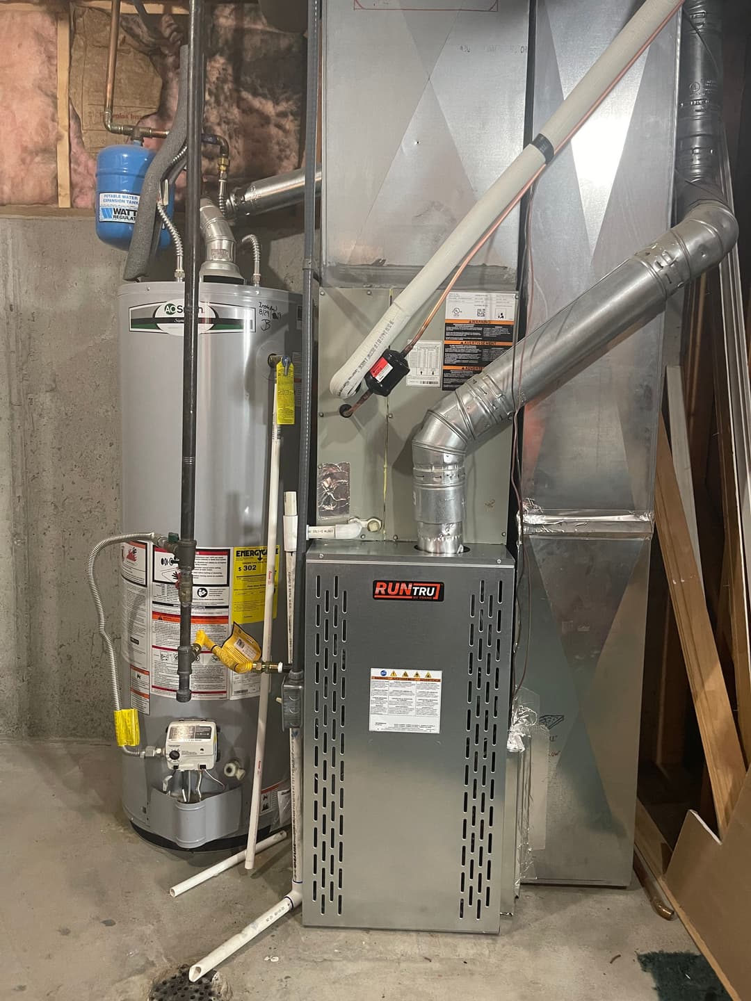 Furnace and water heater installation in a basement with ventilation pipes and insulation.