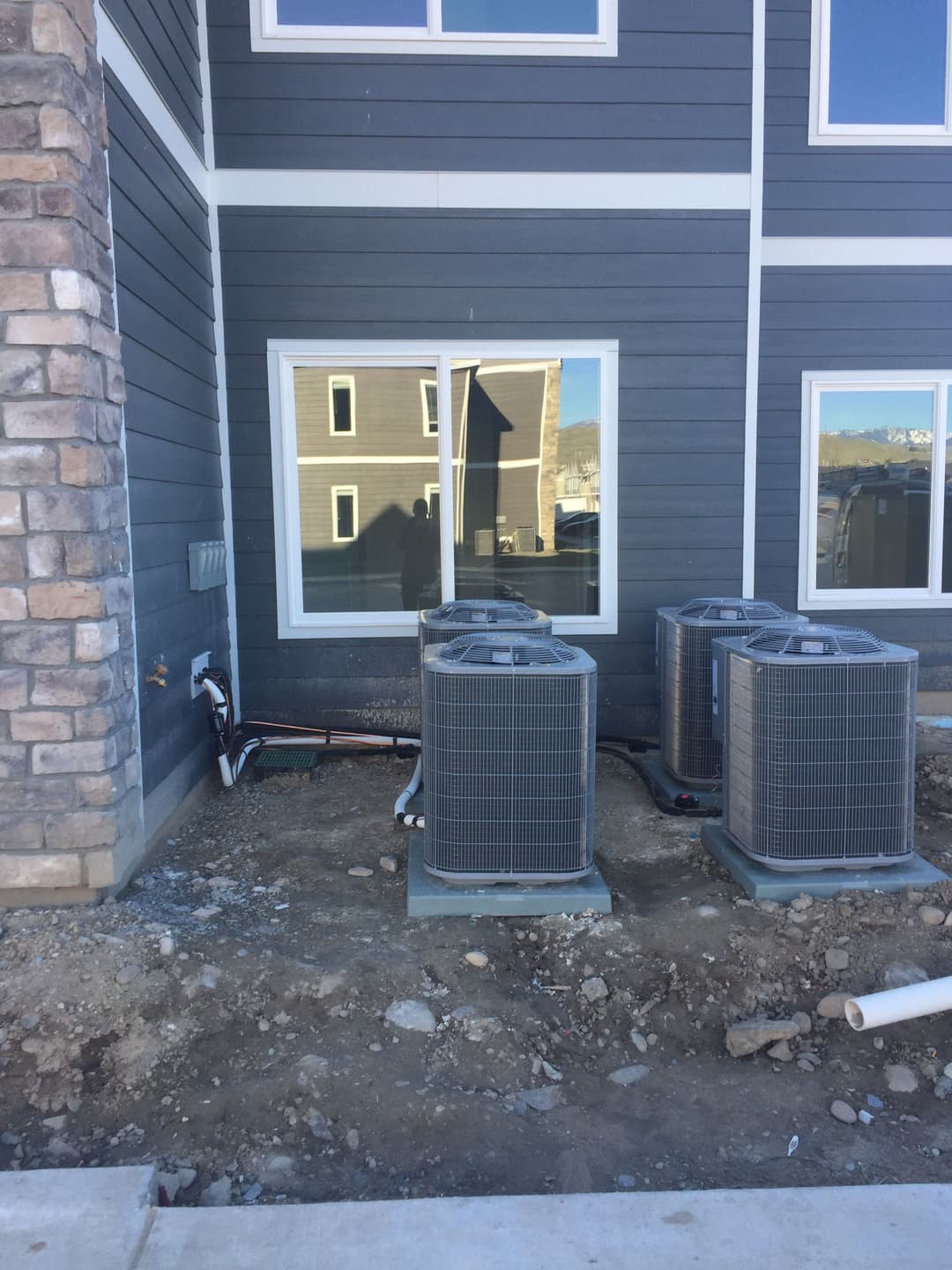 Four air conditioning units installed outside a modern building, with exposed piping and gravel.