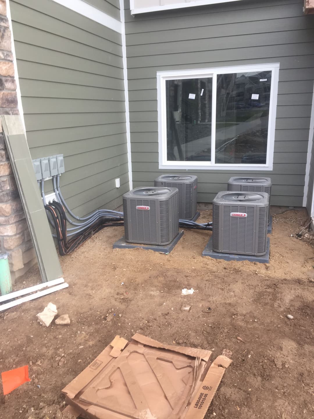 Four air conditioning units installed next to a house with green siding and window.