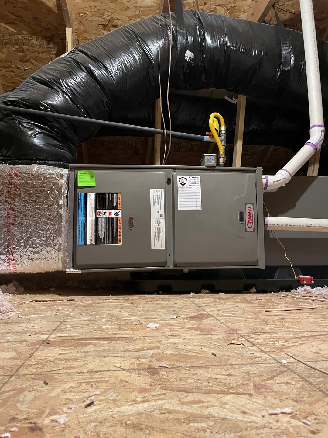 Furnace installation in an attic with insulated ductwork and pipes in a residential setting.