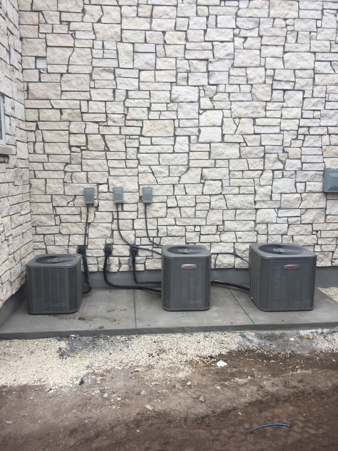 Three air conditioning units installed against a stone wall.